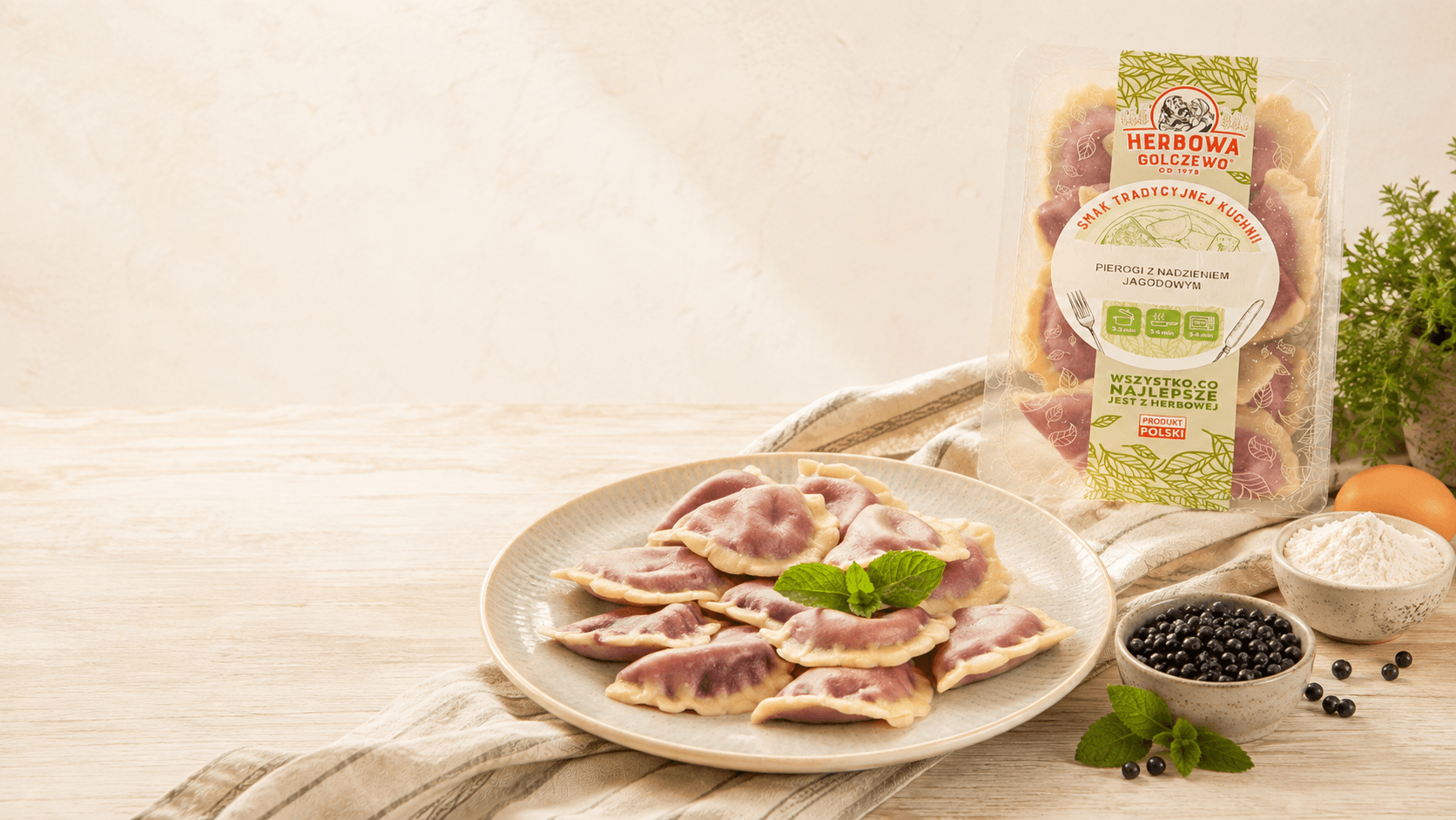 Pierogi z nadzieniem jagodowym Herbowa na talerzu, z opakowaniem i składnikami na jasnym stole.