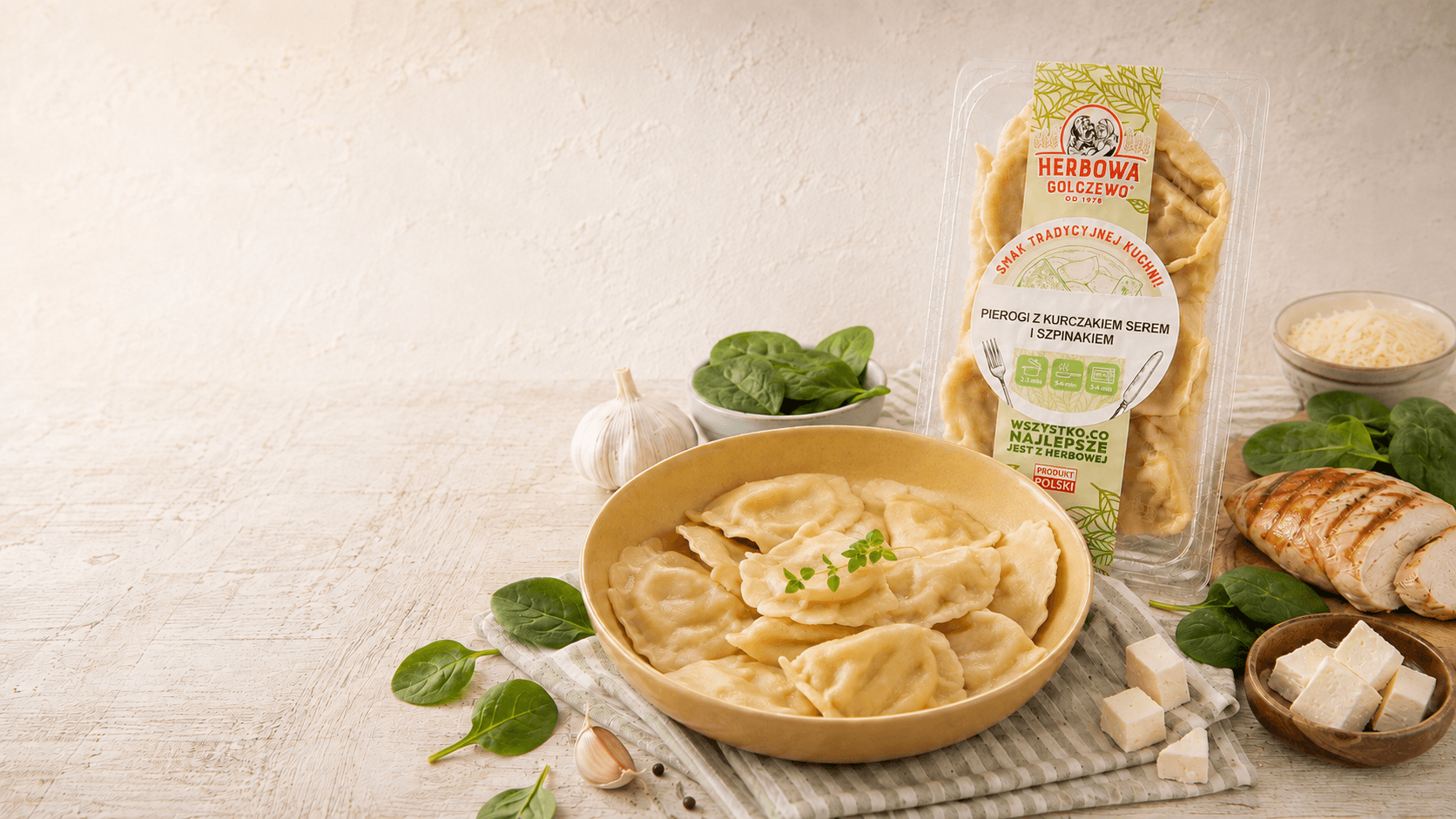 Pierogi z kurczakiem, serem i szpinakiem Herbowa na talerzu, z opakowaniem i składnikami na jasnym stole.