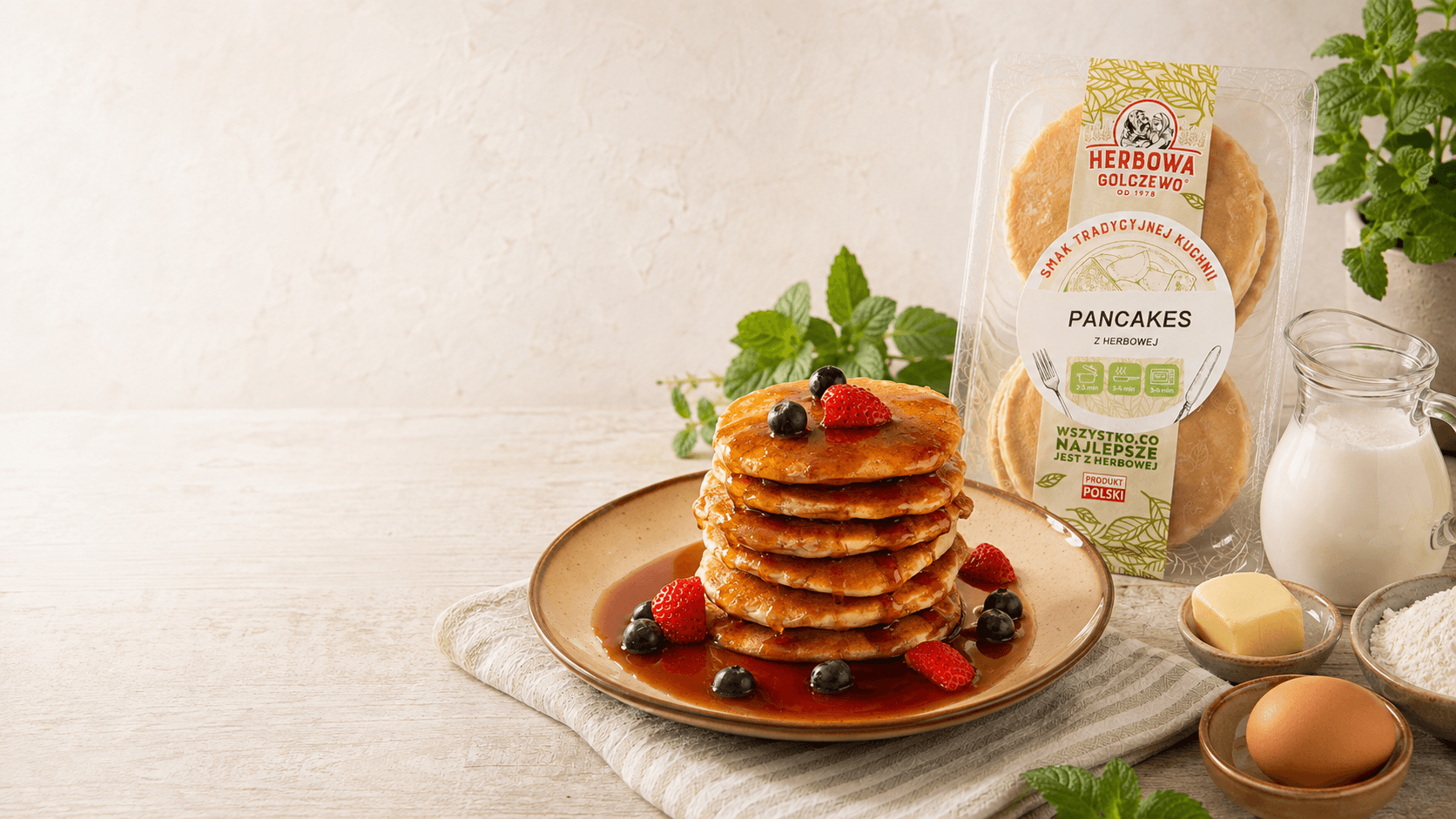 Pancakes z Herbowej Herbowa na talerzu, z opakowaniem i składnikami na jasnym stole.