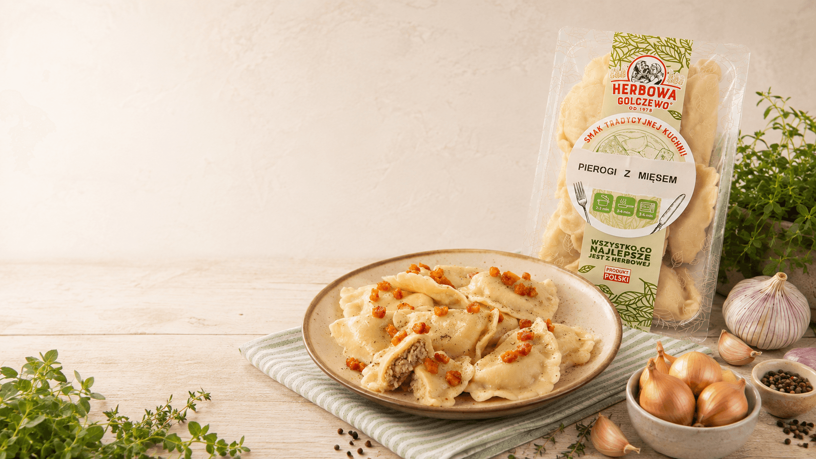 Pierogi z mięsem i dodatkiem wołowiny Herbowa na talerzu, z opakowaniem i składnikami na jasnym stole.
