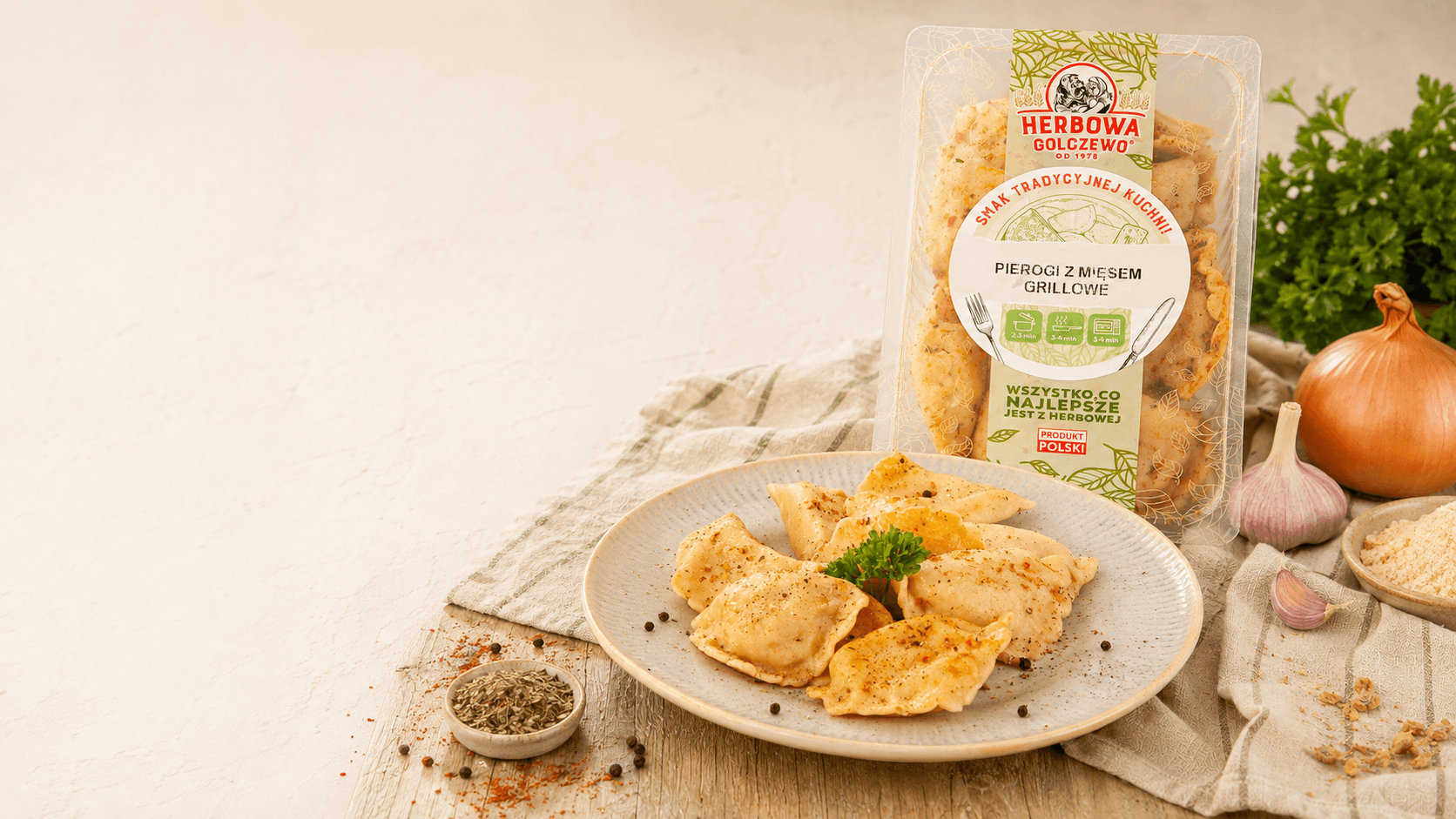 Pierogi z mięsem grillowe Herbowa na talerzu, z opakowaniem i składnikami na jasnym stole.