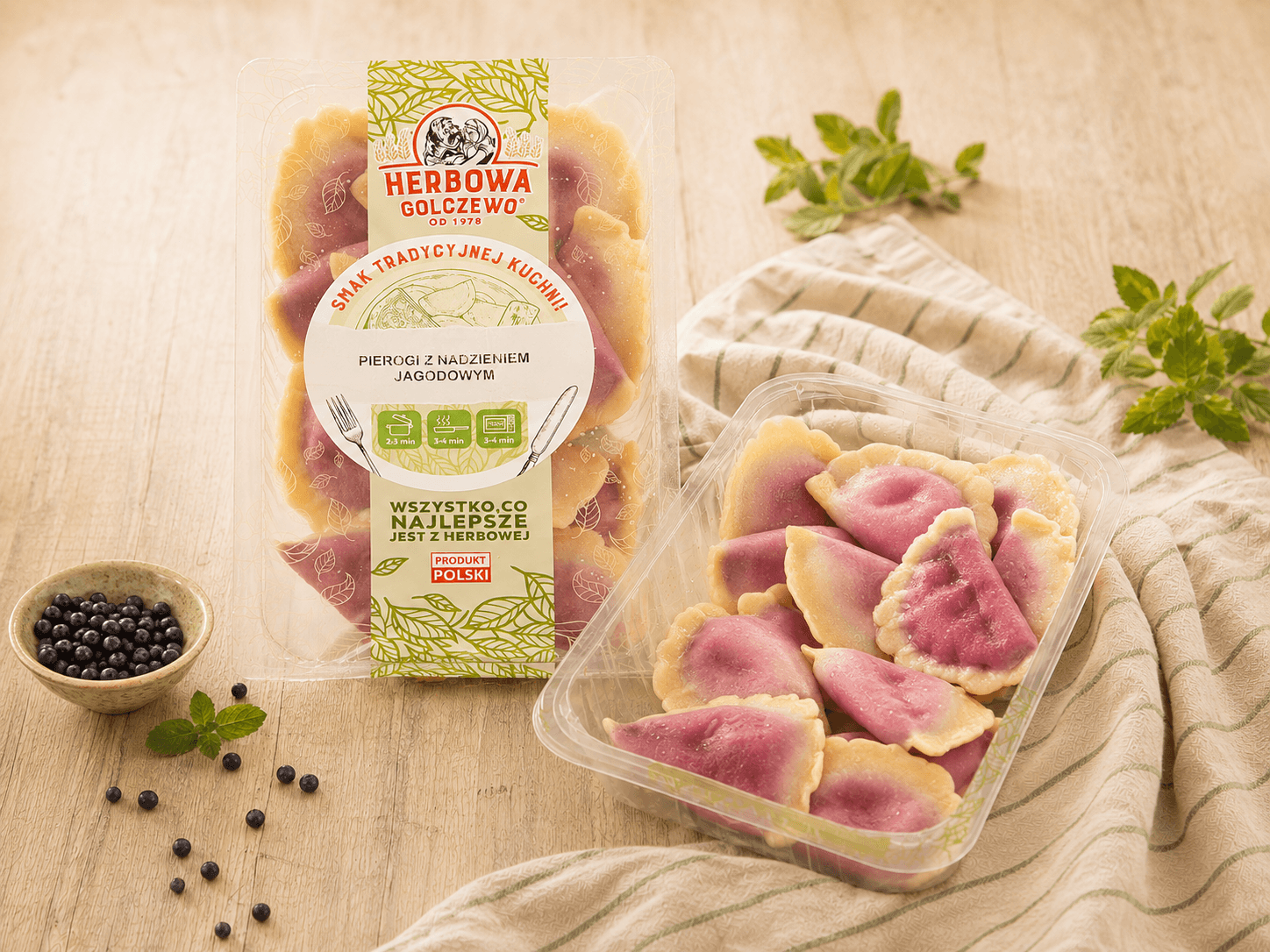 Pierogi z nadzieniem jagodowym Herbowa — zestawienie zamkniętego i otwartego przezroczystego opakowania z dodatkami zgodnymi ze składem.