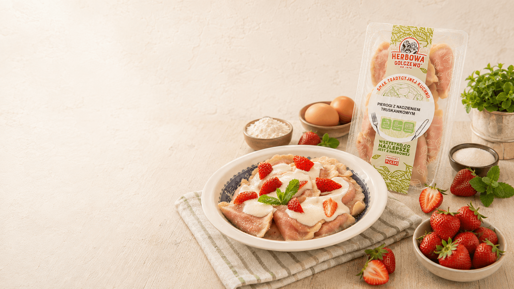 Pierogi z kawałkami truskawek Herbowa na talerzu, z opakowaniem i składnikami na jasnym stole.